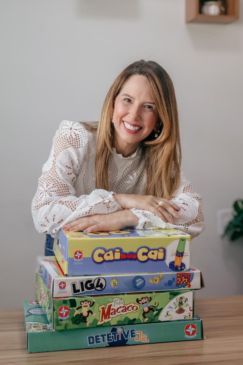 Dra. Ludmila Borges Tenuta, idealizadora do Núcleo Terapêutico Alecrim, sorrindo entre jogos de tabuleiro infantis na clínica