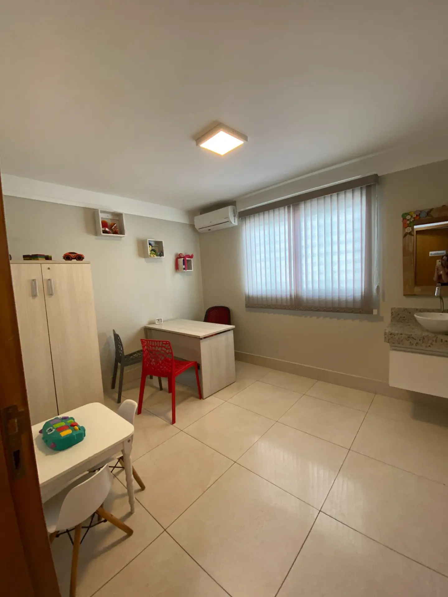 Consultório individual com mesa infantil, cadeiras coloridas, armário e lavatório